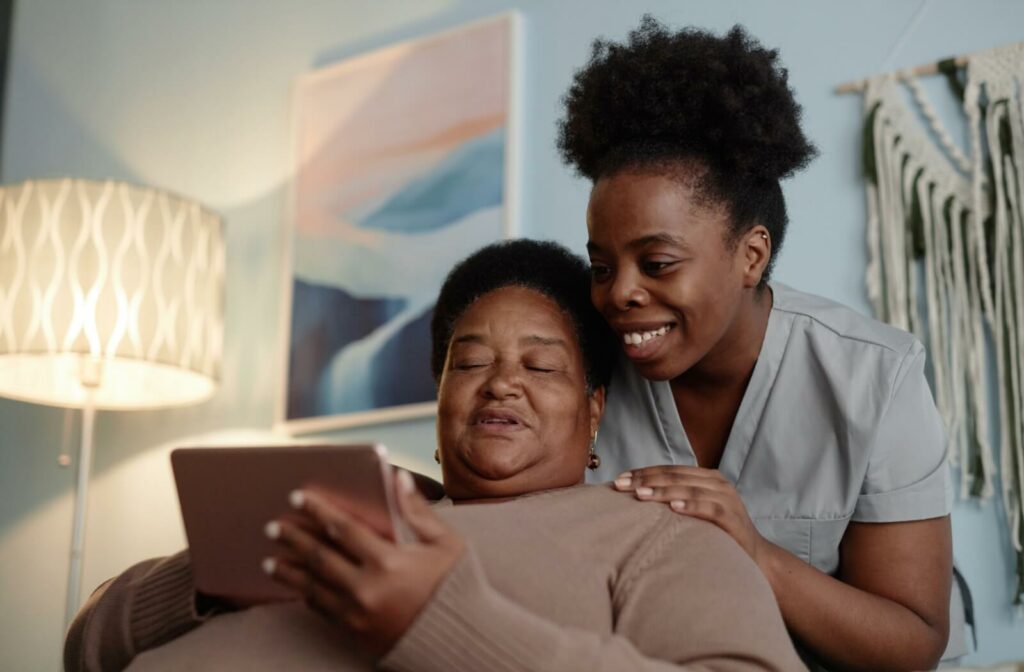 An adult looks over their parent’s shoulder to go over questions written on a tablet to ask during an assisted living tour