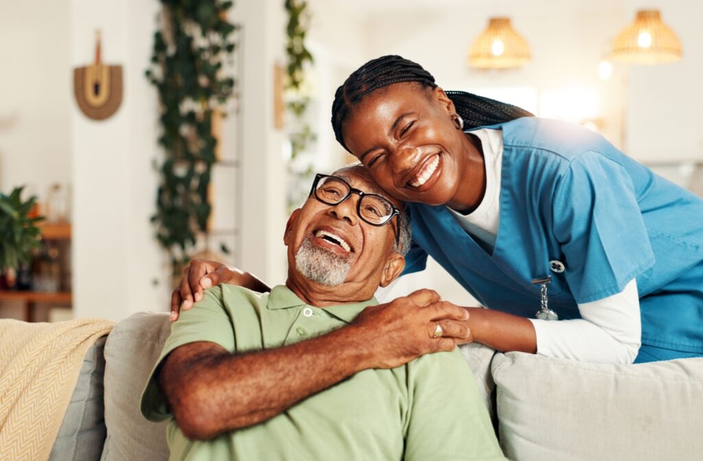 Joyful senior sitting on couch with supportive caregiver smiling closely beside them