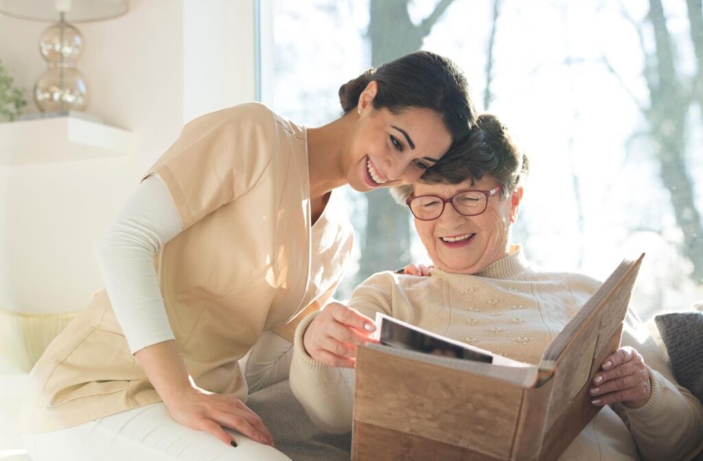 A female caregiver sitting with an elderly woman on the couch, going through a photo album.